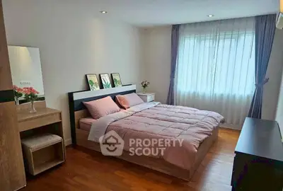 Cozy bedroom with wooden flooring and soft pink bedding, featuring a large window with curtains.