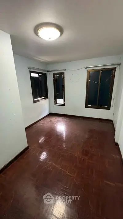 Spacious empty room with wooden flooring and large windows, ideal for customization.