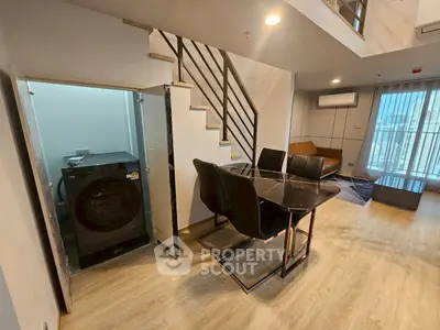 Modern duplex living room with dining area and washing machine, featuring sleek design and ample natural light.