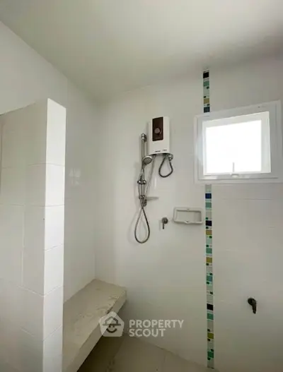Modern bathroom with shower and tiled walls, featuring a small window for natural light.