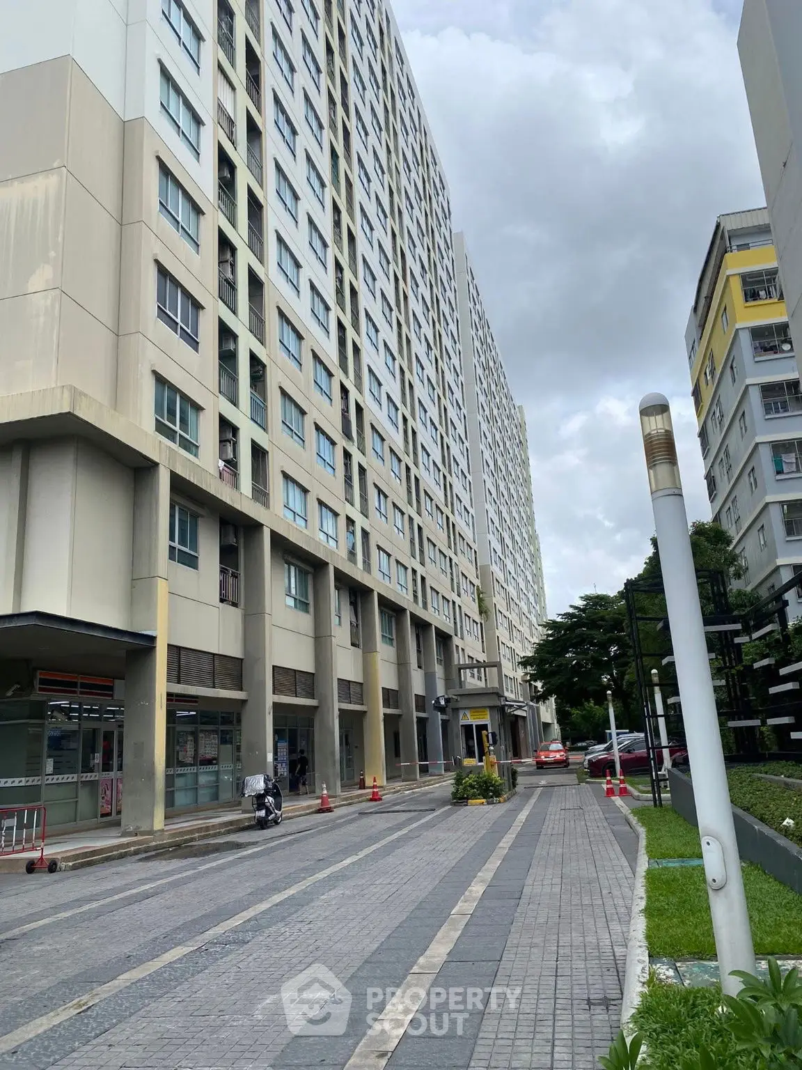 Modern high-rise residential building with spacious walkway and lush greenery.