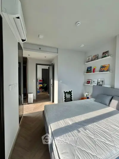 Modern bedroom with stylish decor and natural light, featuring a cozy bed and elegant shelving.