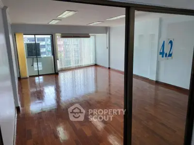 Spacious empty room with polished wooden floors and large windows offering natural light.