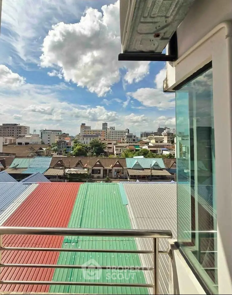 Stunning cityscape view from a modern balcony with colorful rooftops and clear blue sky.