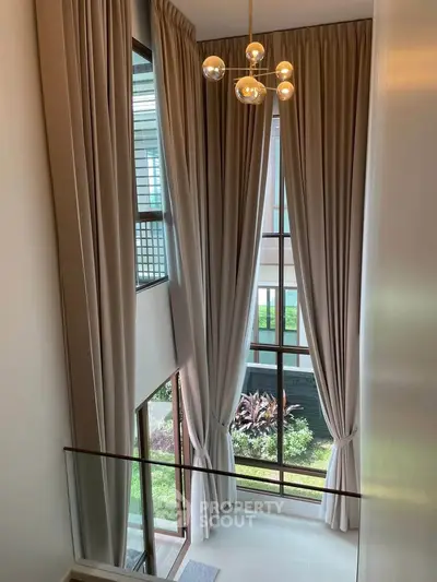 Elegant high-ceiling living area with floor-to-ceiling windows and lush garden view.