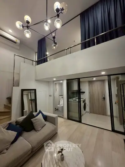 Modern loft apartment with high ceilings and stylish lighting, featuring a cozy living area and a compact laundry space.