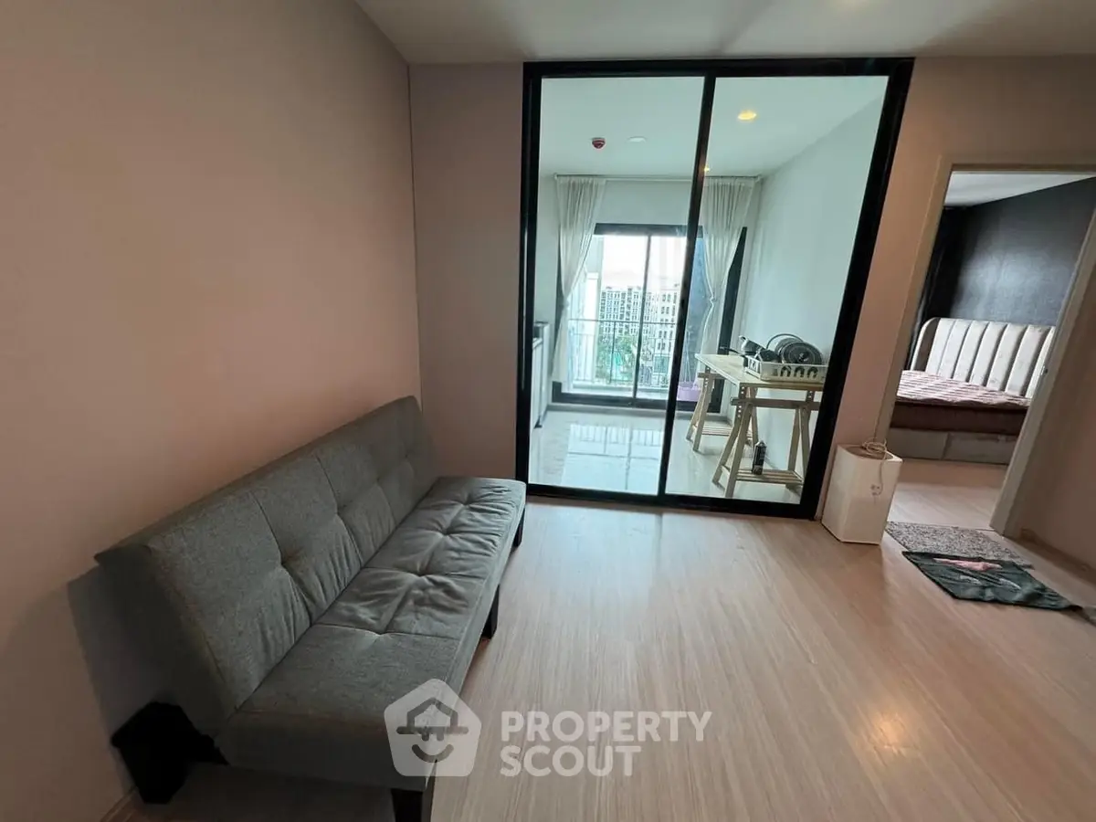 Modern living room with sleek sofa and glass doors leading to a bright balcony, perfect for urban living.