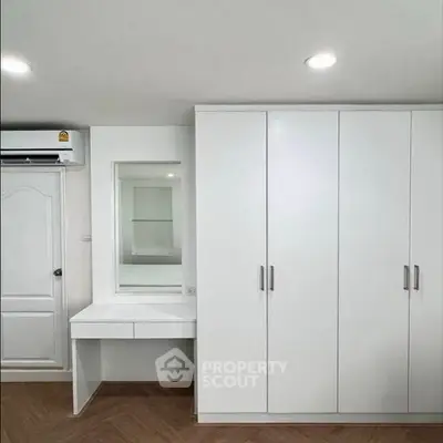 Modern bedroom with white wardrobe and vanity, featuring sleek design and ample storage.