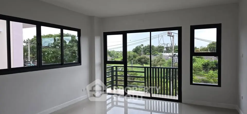 Spacious living room with large windows offering lush green views and abundant natural light.