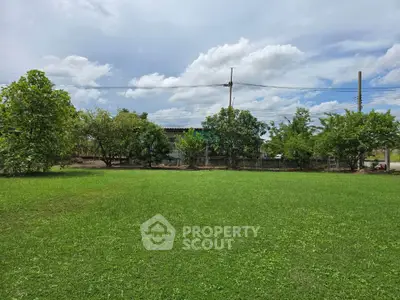 Expansive green lawn with trees and a distant house under a blue sky, perfect for outdoor activities.