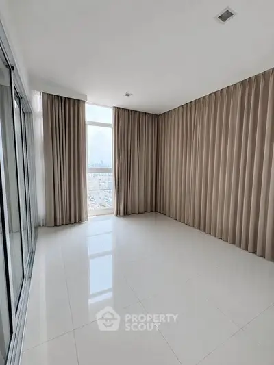 Spacious empty room with large windows and elegant curtains, offering a bright and airy atmosphere.