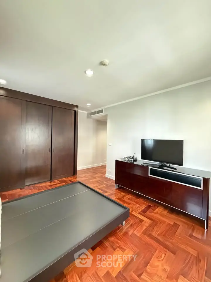 Spacious bedroom with wooden flooring and modern furniture, featuring a sleek TV setup.