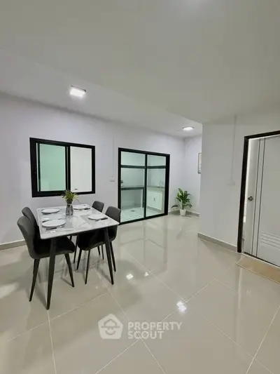 Modern dining area with sleek table and chairs, adjacent to a glass-enclosed space, showcasing minimalist design.