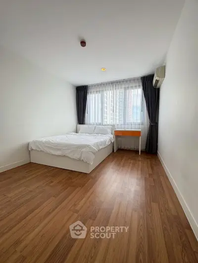 Spacious bedroom with wooden flooring and large window in modern apartment