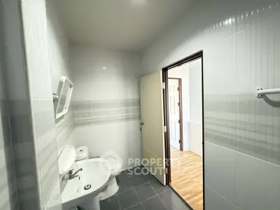 Modern bathroom with sleek white fixtures and tiled walls, leading to a bright hallway.