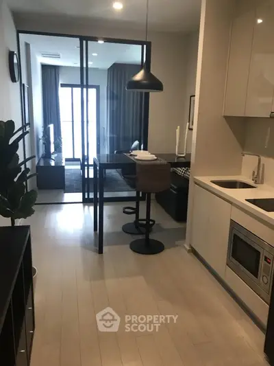 Modern apartment with sleek kitchen and cozy living area, featuring glass partition and stylish decor.