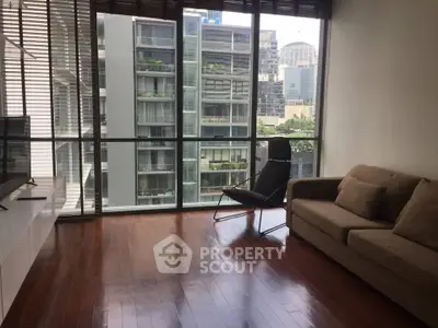 Spacious living room with floor-to-ceiling windows and city view, featuring modern furniture and wooden flooring.