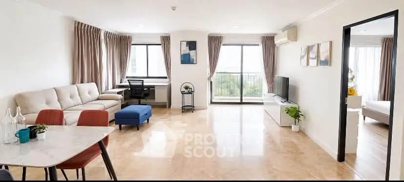 Spacious modern living room with large windows and balcony access, featuring stylish furniture and natural light.