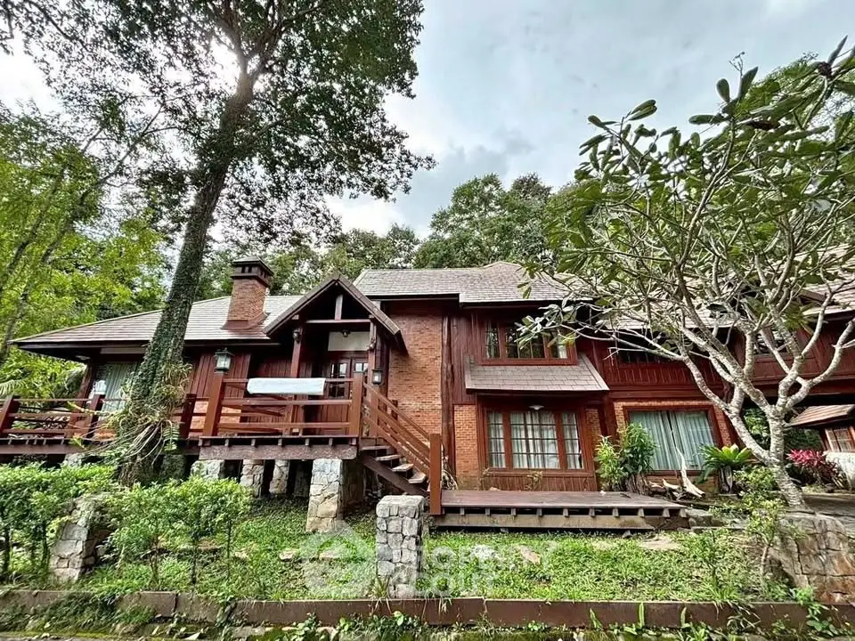 Charming rustic wooden house surrounded by lush greenery, featuring a spacious deck and large windows.