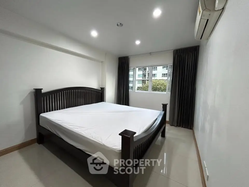 Spacious bedroom with large window and modern furnishings in a well-lit apartment.