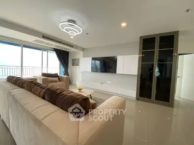 Spacious modern living room with plush sofas and large TV, featuring a balcony view.