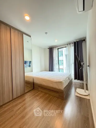 Modern bedroom with wooden flooring, large wardrobe, and wall-mounted TV in a bright apartment.