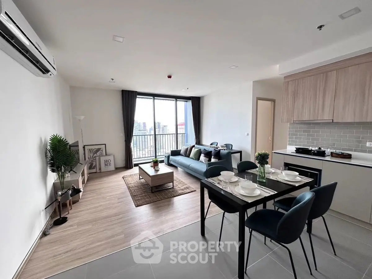 Modern open-layout living room with dining area and city view balcony in a stylish apartment.
