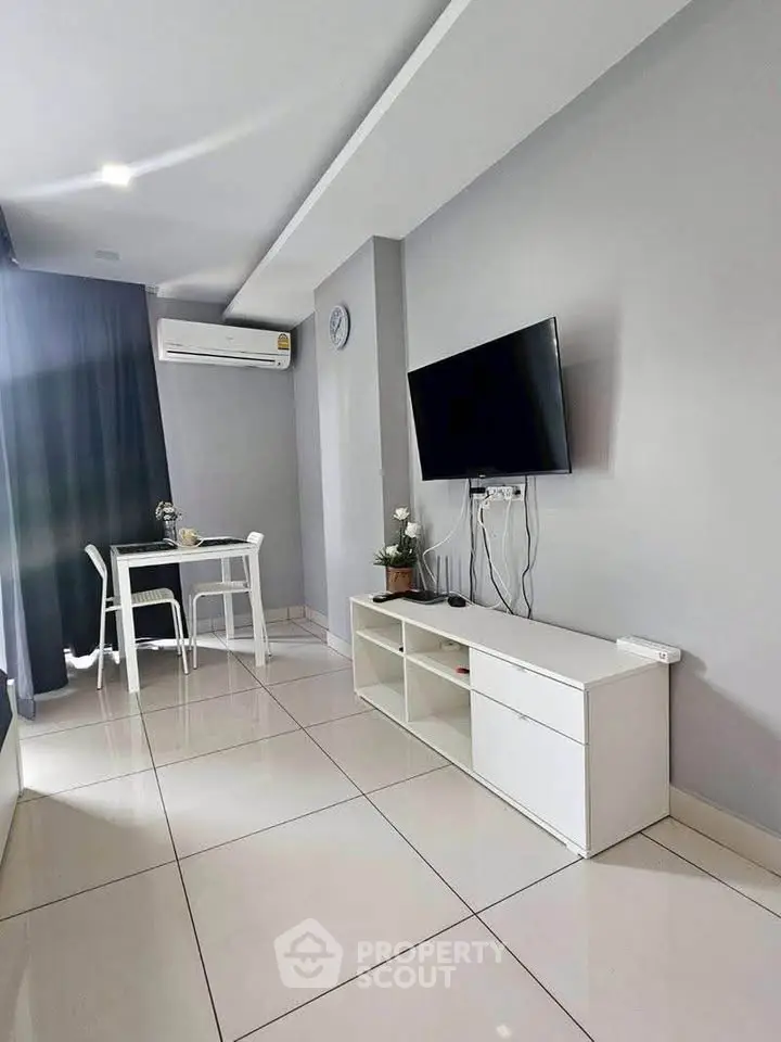 Modern living room with sleek white furniture and wall-mounted TV, featuring minimalist decor and natural light.