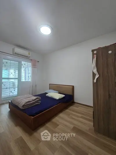 Cozy bedroom with wooden flooring and natural light, featuring a comfortable bed and wardrobe.