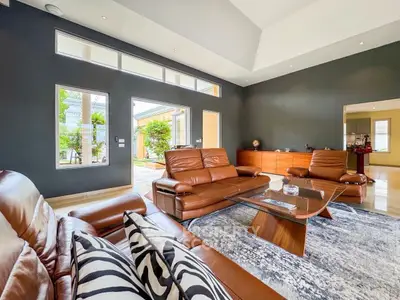 Luxurious living room with leather sofas and modern decor, featuring large windows and high ceilings.