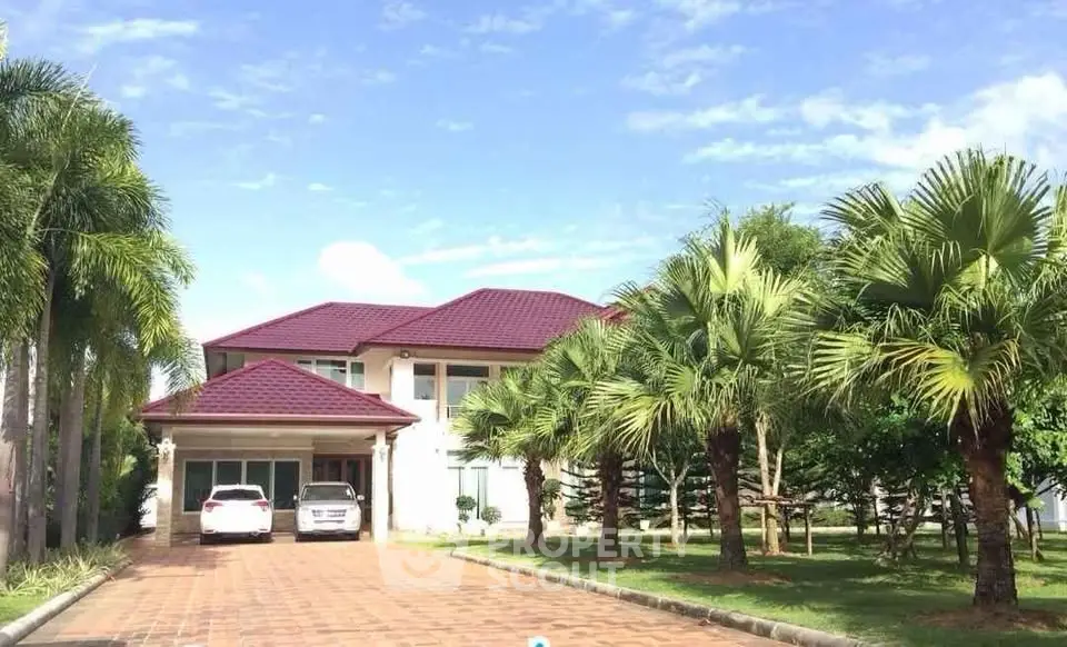 Stunning two-story home with red roof and palm-lined driveway under clear blue sky.