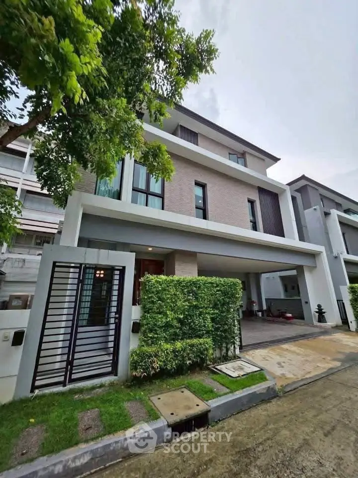 Modern three-story house with lush greenery and sleek design in a suburban neighborhood.