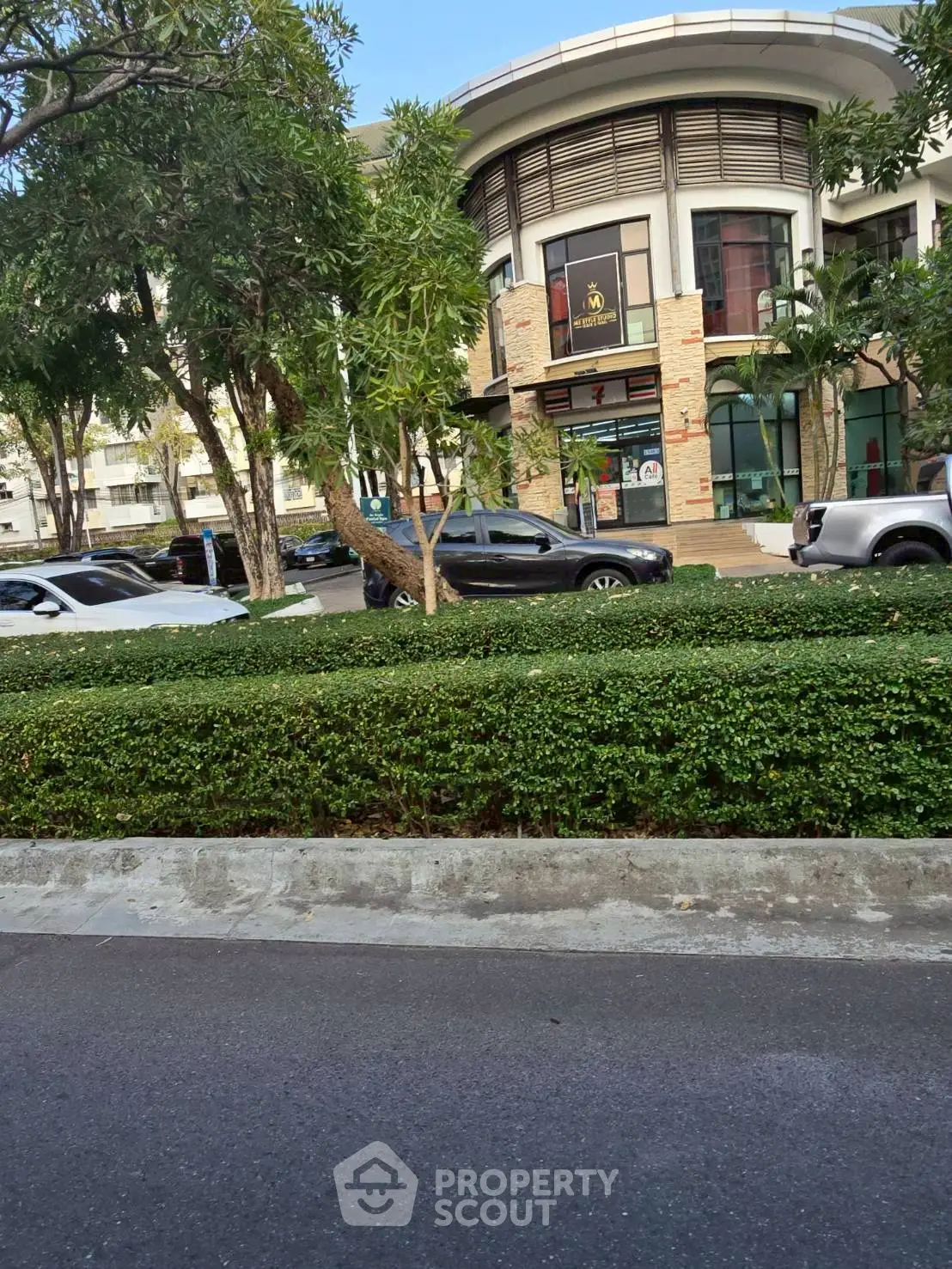 Modern commercial building with lush greenery and parked cars in urban setting.