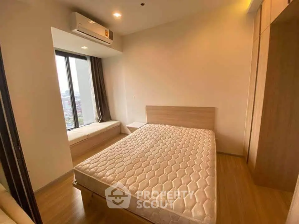Modern bedroom with large window and wooden flooring in a high-rise apartment.