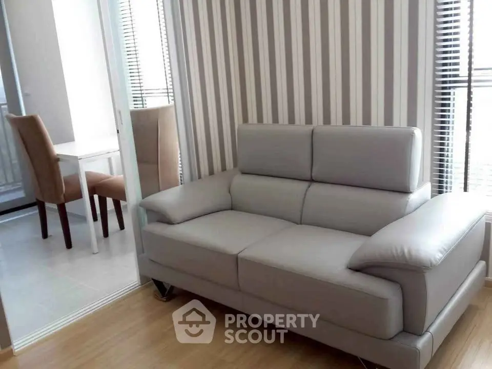 Modern living room with stylish gray sofa and striped wallpaper, adjacent to a dining area with natural light.