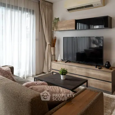 Modern living room with stylish furniture and large TV, featuring natural light and elegant decor.