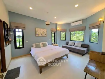 Spacious bedroom with large windows and cozy seating area, offering serene views and modern comfort.