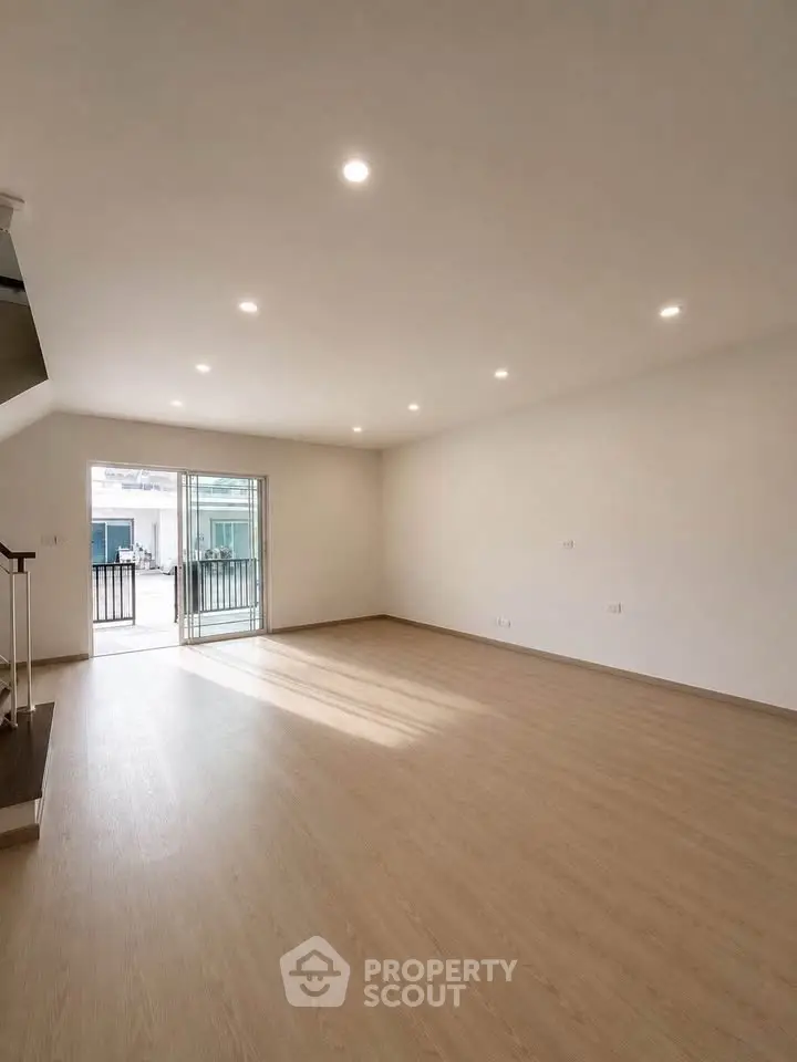 Spacious empty living room with wooden flooring and balcony access