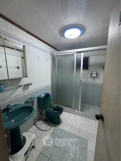 Spacious bathroom with unique green fixtures and frosted glass shower enclosure.