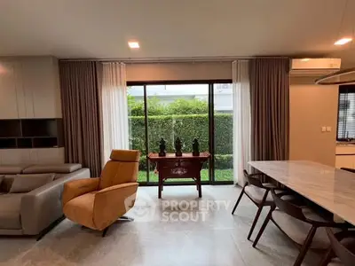 Modern living room with garden view, featuring stylish furniture and large windows.