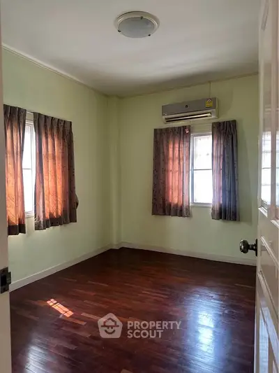 Spacious bedroom with hardwood floors and natural light from two windows.