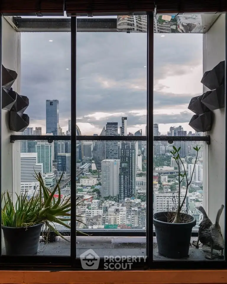 Stunning cityscape view from a high-rise window with potted plants enhancing the urban panorama.
