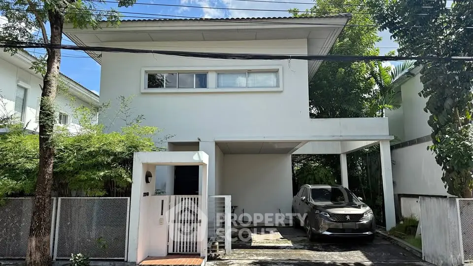 Modern two-story house with carport and lush greenery in a serene neighborhood.