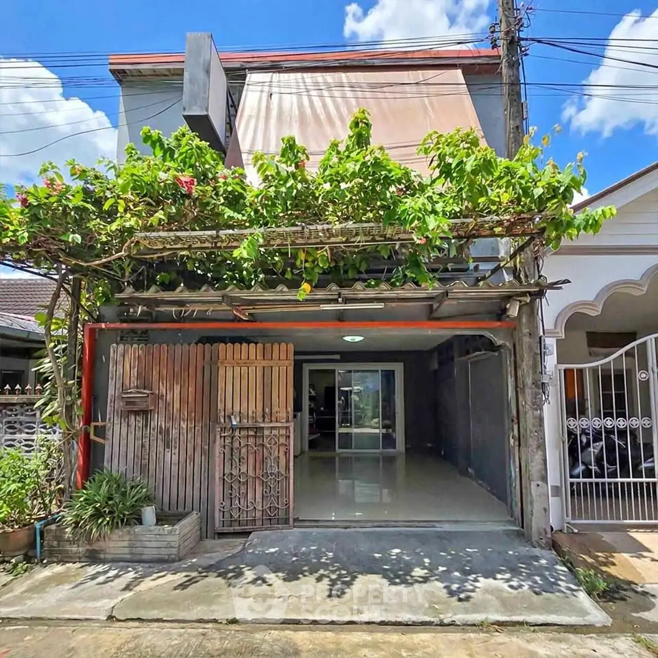 Charming townhouse with vine-covered entrance and spacious driveway in sunny neighborhood.