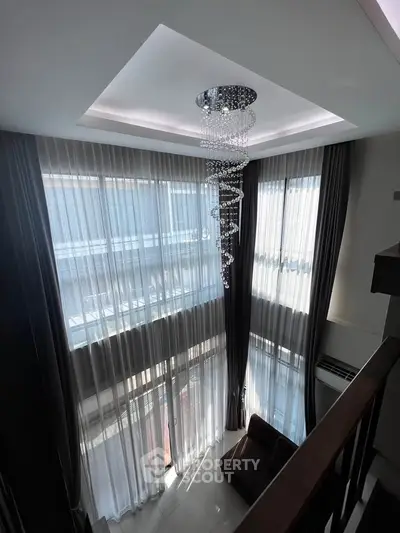 Luxurious high-ceiling living room with elegant chandelier and floor-to-ceiling windows.