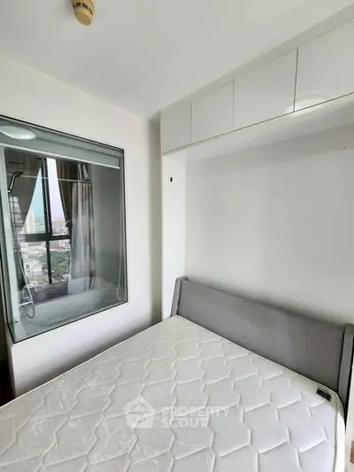 Modern bedroom with city view and built-in storage, featuring a comfortable bed and large window.