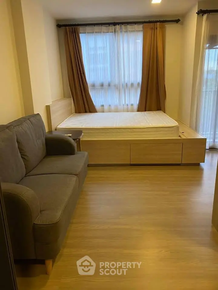 Cozy bedroom with wooden flooring, bed, and sofa, featuring large windows with curtains.