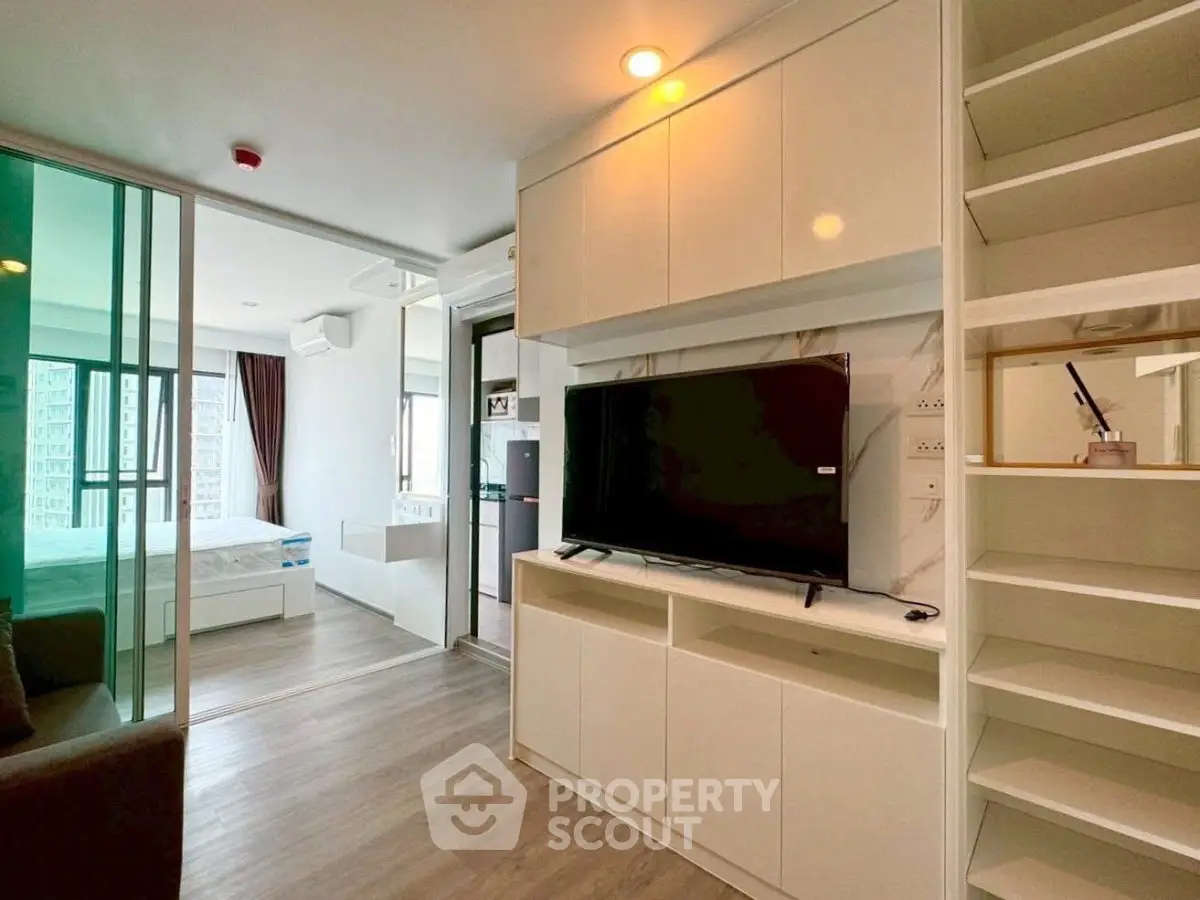 Modern apartment interior with open living room and bedroom, featuring sleek furniture and large windows.