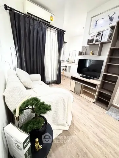 Cozy living room with modern decor and natural light, featuring a TV and stylish shelving.