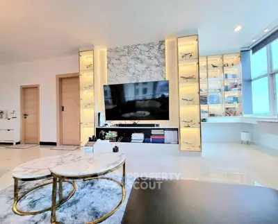 Luxurious modern living room with marble accents and large TV, featuring elegant decor and ample natural light.